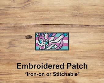 May include: Embroidered patch featuring a stylized creature with pink, white, blue, and teal colors. The patch has a rectangular shape with a teal border. Text on the image reads "Embroidered Patch *Iron-on or Stitchable*".