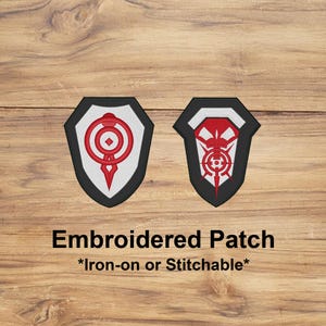 May include: Two embroidered patches with shield shapes. One features a red design on a white background, the other has a red design on a white background. Both are outlined in black. The text "Embroidered Patch" and "*Iron-on or Stitchable*" are below the patches.