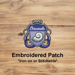 May include: Embroidered patch featuring a shield design with the word "Octavinelle" and a seashell. The patch has a purple and white color scheme with blue tentacles. The text "Embroidered Patch" and "*Iron-on or Stitchable*" are below the shield.