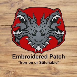 May include: Embroidered patch featuring a two-headed dog design with sharp teeth and a spiked collar, set against a red background. The patch has the words "Embroidered Patch" and "*Iron-on or Stitchable*" in black text.