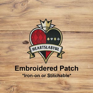 May include: Embroidered patch with a heart-shaped design, split into red diamond and black spade sections. The patch features a banner with the text "HEARTSLABYUL" and a gold crown. The text "Embroidered Patch *Iron-on or Stitchable*" is below.