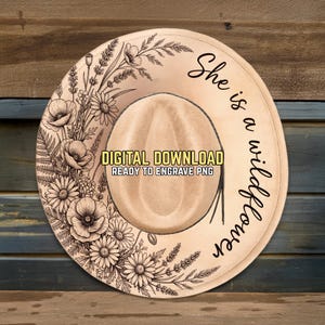 May include: A beige cowboy hat with a floral design and the text "She is a wildflower." The hat features a detailed illustration of flowers and foliage around the brim. The image also includes the text "DIGITAL DOWNLOAD READY TO ENGRAVE PNG."
