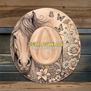 Puede incluir: Diseño de sombrero de vaquero beige con una detallada ilustración de la cabeza de un caballo en el lado izquierdo, rodeada de motivos florales y mariposas. El texto "DIGITAL DOWNLOAD READY TO ENGRAVE PNG" se muestra en la corona del sombrero. Fondo de madera.