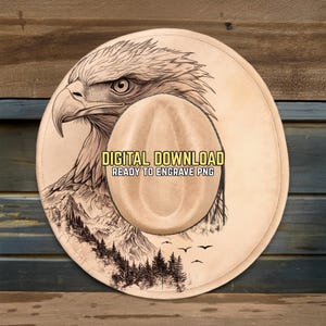 Puede incluir: Diseño de sombrero de vaquero beige con una ilustración detallada de la cabeza de un águila, montañas y árboles. El texto "DIGITAL DOWNLOAD READY TO ENGRAVE PNG" se muestra en el sombrero. Adecuado para grabar.