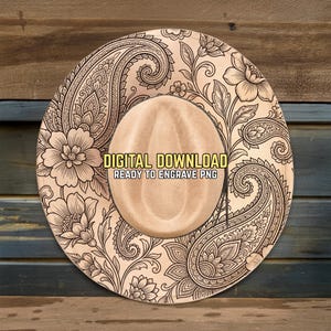 May include: A tan cowboy hat with an intricate paisley and floral design. The hat features the text "DIGITAL DOWNLOAD READY TO ENGRAVE PNG". The hat is set against a wooden background.
