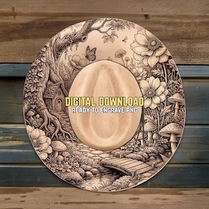 May include: A round, light brown wooden design with a central oval shape. The design features a detailed illustration of a forest scene with a small house, flowers, mushrooms, and a bridge. Text reads "DIGITAL DOWNLOAD READY TO ENGRAVE PNG."