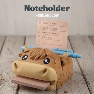 May include: A brown and tan Highland cow-shaped notecard holder with a light blue pen and a pink notepad. The notepad has a list with the text "PLANT A TREE", "BUILD A HOUSE", "RAISE A CHILD", and "GET A DOG".