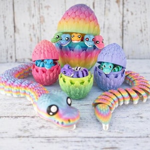 May include: A collection of colorful, 3D-printed dragon toys. The set includes several dragon eggs in pink, purple, and blue, each with a baby dragon inside. Two rainbow-colored dragon snakes are also present, along with a large, multi-colored dragon egg.