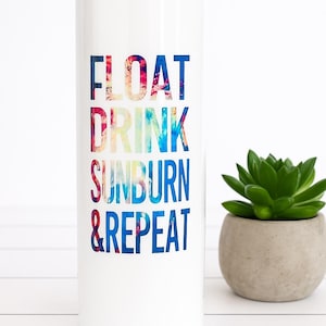 May include: White tumbler with the words "FLOAT DRINK SUNBURN & REPEAT" in colorful text. A small succulent in a gray pot sits to the right of the tumbler. The tumbler is cylindrical and appears to be made of metal.