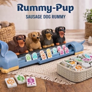 May include: A board game called "Rummy-Pup" with a dachshund theme. The game includes a blue dachshund-shaped game board, dachshund game pieces, and numbered tiles. The game's name is displayed in a playful font at the top of the image.