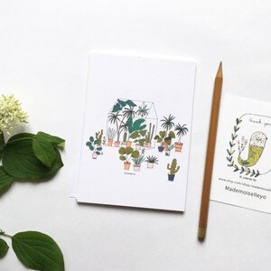May include: A white card with a hand-drawn illustration of a greenhouse filled with potted plants. The plants are drawn in various shades of green, brown, and orange. The greenhouse is outlined in black and has a white roof. The card has the text "Mademoiselleyo" at the bottom.