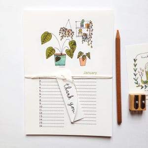 Peut inclure: Un calendrier blanc avec une illustration dessinée à la main de plantes en pot et une plante suspendue. Le calendrier est pour janvier et a une petite étiquette qui dit "merci".