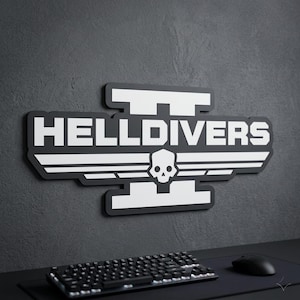 Può includere: Un cartello in bianco e nero con la scritta "HELLDIVERS" in grassetto, un teschio e forme alate. Il cartello è montato su un muro grigio scuro. Una tastiera e un mouse neri sono in primo piano.
