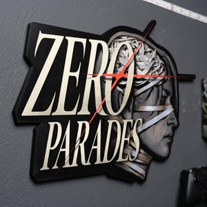 Peut inclure: Une enseigne murale noire avec le texte blanc ZERO PARADES dans une police stylisée. À droite, une illustration de profil d'une tête enveloppée de bandages est visible, avec une fine ligne rouge traversant le design en diagonale au centre.