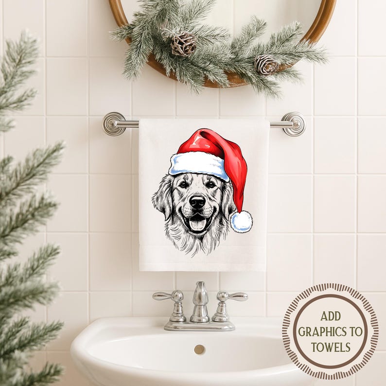 Op de afbeelding: Witte handdoek met een gedetailleerde illustratie van een Golden Retriever met een rode kerstmuts. De handdoek hangt aan een zilveren stang boven een witte wastafel. Boven de handdoek hangt een decoratieve krans.