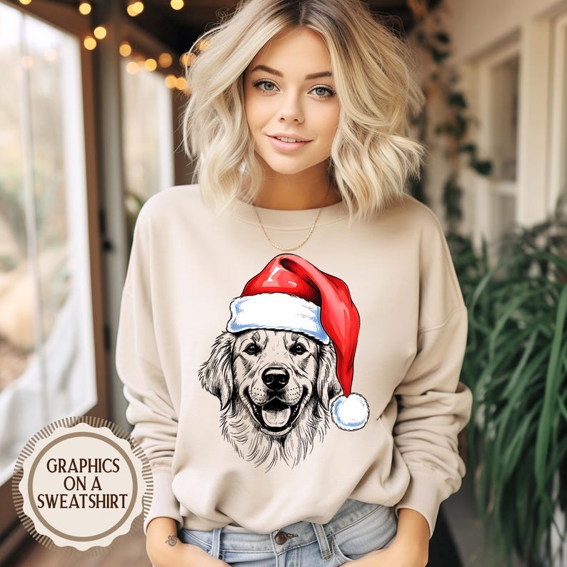 Op de afbeelding: Beige sweatshirt met een afbeelding van een Golden Retriever met een kerstmuts. De hond is afgebeeld in zwart-wit, met een rood-witte kerstmuts. De tekst "GRAPHICS ON A SWEATSHIRT" is gedrukt op een cirkelvormig label.