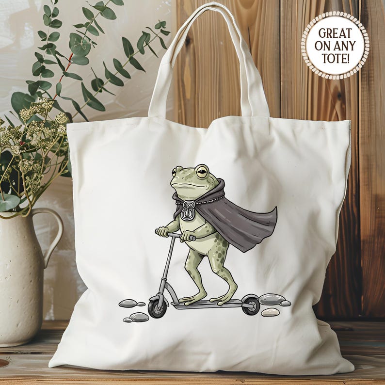 K&ouml;nnte beinhalten: Wei&szlig;er Stoffbeutel mit einem Cartoon-Frosch auf einem Roller. Der Frosch tr&auml;gt einen dunkelgrauen Umhang und ein Medaillon. Die Tasche hat einen Griff und den Text "GREAT ON ANY TOTE!" in einem Kreis.