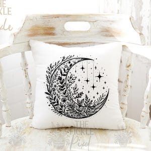 May include: A white pillow with a black and white illustration of a crescent moon with floral designs and stars. The moon is surrounded by leaves and flowers.