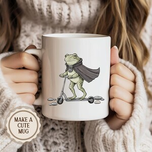 K&ouml;nnte beinhalten: Wei&szlig;e Keramik-Tasse mit einem Cartoon-Frosch, der einen Umhang tr&auml;gt und einen Roller f&auml;hrt. Der Frosch ist gr&uuml;n mit einem grauen Umhang und f&auml;hrt einen grauen Roller. Die Tasse hat einen wei&szlig;en Griff und den Text "MAKE A CUTE MUG" an der Seite.