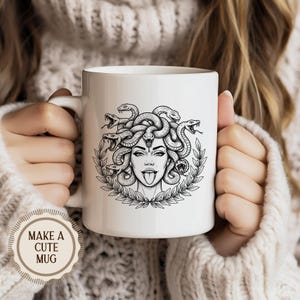 May include: White ceramic mug featuring a black and white illustration of Medusa with snakes for hair, a laurel wreath, and her tongue sticking out. The mug has a handle and the text "MAKE A CUTE MUG" on a sticker.