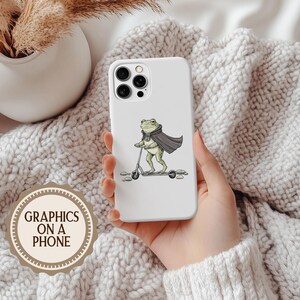 K&ouml;nnte beinhalten: Wei&szlig;es Handycase mit einem Cartoon-Frosch auf einem Roller, der einen Umhang und einen Schal tr&auml;gt. Das Case hat einen Ausschnitt f&uuml;r eine Dreifach-Kamera. Der Text "GRAPHICS ON A PHONE" befindet sich auf einem runden Aufkleber unten links.