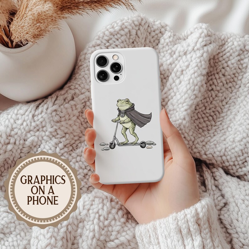 K&ouml;nnte beinhalten: Wei&szlig;es Handycase mit einem Cartoon-Frosch auf einem Roller, der einen Umhang und einen Schal tr&auml;gt. Das Case hat einen Ausschnitt f&uuml;r eine Dreifach-Kamera. Der Text "GRAPHICS ON A PHONE" befindet sich auf einem runden Aufkleber unten links.