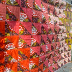 May include: A patchwork quilt with a geometric pattern of triangles in shades of orange, pink, brown, and green. The quilt is made of different fabrics with floral designs.