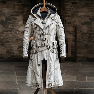 May include: An off-white leather coat with a hooded design. The coat has multiple buckles, straps, and decorative stitching. It is displayed on a wooden hanger and mannequin, highlighting its intricate details and craftsmanship. The coat's length is visible.