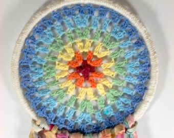 Puede incluir: Un atrapasueños de crochet arcoíris con un aro blanco y borlas de tela de colores.