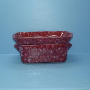 May include: A set of two square ceramic planters in a speckled burgundy color. The planters are nested together.