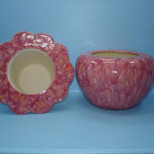 May include: A two-piece ceramic container set featuring a scalloped lid and a rounded bowl. Both pieces have a glossy, mottled glaze in shades of pink, magenta, and cream, with a smooth, solid cream-colored interior finish on both components.