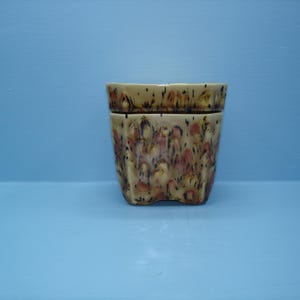 May include: A ceramic planter with a fluted, cylindrical body featuring a speckled glaze in shades of cream, tan, and reddish-brown. The surface has a textured appearance with dark brown and black flecks distributed across the exterior.