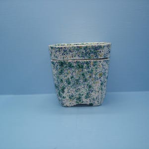 May include: A ceramic planter with a white base featuring a speckled pattern of blue, green, and yellow dots. The vessel has a rectangular shape with rounded corners and a distinct horizontal ridge separating the upper rim from the main body.