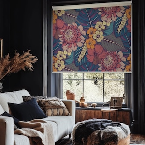 May include: A white couch with pillows and a throw blanket in a living room with a window covered by a floral patterned roller shade. The shade features a vibrant tropical print with pink, yellow, and orange flowers on a dark blue background.