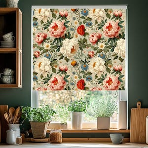May include: A floral patterned roller shade featuring large pink, red, and white peony blooms with green leaves and small blue and yellow flowers. The shade is installed in a kitchen window, with plants on the windowsill.