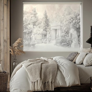 Könnte beinhalten: Ein weißes Bett mit einem weißen Bettbezug und einer beigefarbenen Strickdecke mit Fransen. Das Bett steht in einem Schlafzimmer mit einem Fenster dahinter. Das Fenster hat einen weißen Rollladen mit einer Schwarzweißzeichnung einer Gartenszene mit einem Gebäude im Hintergrund.