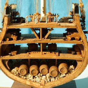 Puede incluir: Un modelo de barco de madera cortado por la mitad, revelando el interior. El casco del barco está hecho de madera y tiene varias cubiertas. La cubierta inferior está llena de barriles, mientras que las cubiertas superiores presentan cañones y otros detalles del barco.