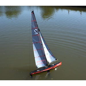 Op de afbeelding: Een zwart en rood radiografisch zeilboot met een wit zeil waarop het nummer "2" en het woord "FOCUS" is gedrukt. De zeilboot drijft op een wateroppervlak.