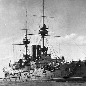 Puede incluir: Una fotografía en blanco y negro de un gran barco de guerra histórico con múltiples mástiles y una gran cubierta. El barco está en el mar y el agua está tranquila.