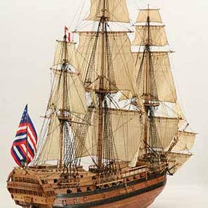 May include: A detailed wooden model of a sailing ship with white sails and a black and red American flag. The ship has a wooden hull and a deck with intricate details.
