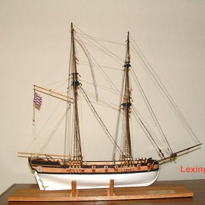 May include: A detailed model of a wooden sailing ship, the Lexington, with white sails and a black hull. The ship is on a wooden base and has a small American flag flying from the mast.