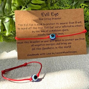May include: A red string bracelet featuring an evil eye charm. The charm is blue with a black center. The bracelet is shown with a card that reads "Evil Eye Red String Bracelet". The card also includes text about the bracelet's purpose.