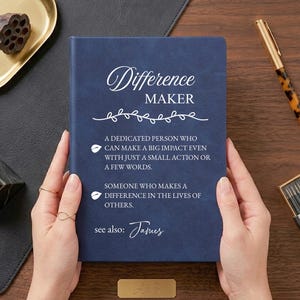 May include: A dark blue notebook with white text that reads: Difference MAKER, A dedicated person who can make a big impact even with just a small action or a few words. Someone who makes a difference in the lives of others. see also: James.
