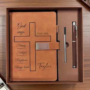 Può includere: Un set regalo in scatola con un diario in pelle marrone con un design a croce e le parole "Dio dice TU SEI" e testo ispiratore. Include una penna abbinata e una penna sottile argentata. Il diario è personalizzato con il nome "Taylor".
