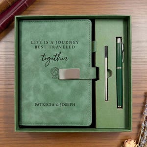 May include: A sage green journal set in a matching box, featuring a metal clasp and the text "LIFE IS A JOURNEY BEST TRAVELED together" with a globe icon and the names "PATRICIA & JOSEPH". The set includes a matching green pen and a refill cartridge.