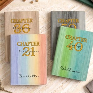 Puede incluir: Tres diarios rectangulares con cubiertas texturizadas. Uno es marrón claro con 'CHAPTER 36' en dorado. Uno es gris con 'CHAPTER 50' en dorado. Uno es degradado arcoíris con 'CHAPTER 21' y 'Charlotte' en negro. Uno es verde con 'CHAPTER 40' y 'William' en negro.