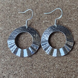 Peut inclure: Une paire de boucles d'oreilles argentées en forme de cerceau. Les boucles d'oreilles présentent une texture martelée sur le cercle extérieur et un motif strié sur le bord intérieur. Elles sont suspendues à un simple crochet.