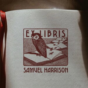 May include: An open book with a red ribbon bookmark. The page displays a red and brown illustration of an owl on a book, with the text "EX LIBRIS" and "SAMUEL HARRISON".
