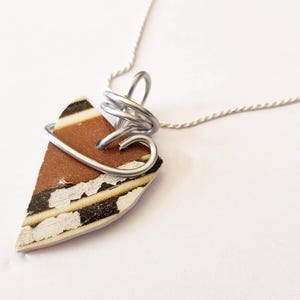May include: A handmade pendant necklace featuring a triangular piece with brown, black, and white patterns, wrapped in silver-colored wire. The pendant hangs from a delicate silver chain, creating a unique and artistic accessory.