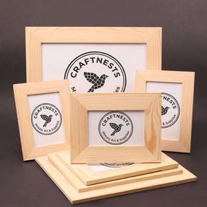 May include: A collection of unfinished wooden picture frames in various sizes. Each frame surrounds a white insert with the "CRAFTNESTS" logo, featuring a bird graphic and the words "Mosaic Art & Supplies". The frames are stacked and arranged on a dark surface.